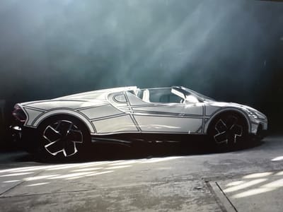 A white convertible sports car with black line art accents is parked on a concrete floor. The car has a low profile and a sleek, aerodynamic design. The wheels are black with a unique, star-shaped design. The background is dark and smoky, with a faint light source from the top left, casting shadows on the floor. There is no indication of the car's location in Sant'Angelo di Piove di Sacco, Italy.