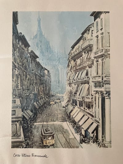This is a watercolor painting depicting an architectural scene, likely a street or piazza in a European city. The perspective is unusual, looking down at an angle that suggests the viewer is on a higher elevation or the image is rotated.
The primary subjects are the buildings lining what appears to be a street. These structures are rendered in muted tones of grey, white, and blue, with a sense of depth created by the detailed rendering of their facades, windows, and architectural elements like columns and cornices. The buildings are densely packed, creating a sense of urban density.
In the foreground, or what would be the foreground if the image were right-side up, there are what appear to be cable cars or trams suspended on wires, moving along the street. These vehicles are depicted as boxy structures with visible windows. The street itself is paved, and there are some scattered dark masses that could represent debris, trees, or shadows.
The sky is a pale blue, with some soft, watercolor-like clouds. The lighting suggests it is daytime, perhaps late morning or afternoon, with gentle illumination. There are no people clearly visible, contributing to a sense of quiet or perhaps the absence of immediate activity.
A notable detail is the handwritten text on the right side of the painting: "Corso Vittorio Emanuele". This is a common street name in Italy, and its presence, along with the architectural style, strongly suggests an Italian setting. The overall emotion evoked is one of historical charm and architectural appreciation.