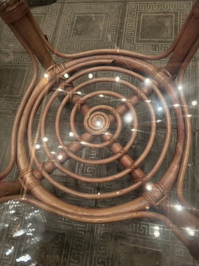 The image shows the underside of a rattan chair. The chair has a circular design with concentric rings of rattan, tied together with smaller pieces of rattan. The chair is placed on a tiled floor with a geometric pattern. The scene is likely indoors. The image does not provide any information about the location in Chuguyevka, Russia.