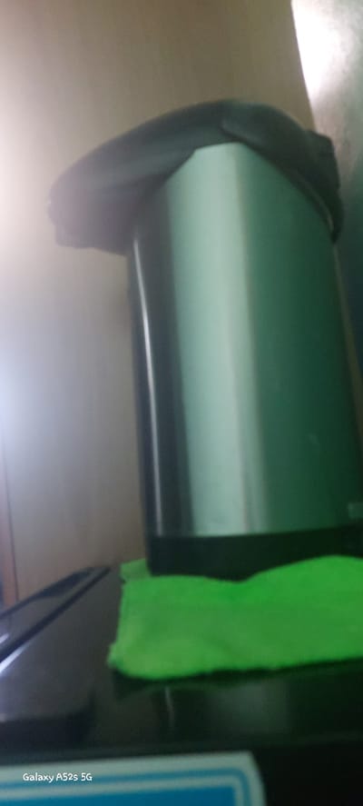 The image shows a close-up view of a silver thermos with a black lid. A bright green cloth is placed on a black surface in front of the thermos. The background is blurred and appears to be a wall. The text "Galaxy A52s 5G" is visible in the bottom left corner, indicating the device used to capture the image. There is no information in the image that would allow for its location to be determined in Nikolayevsk-on-Amur, Russia.