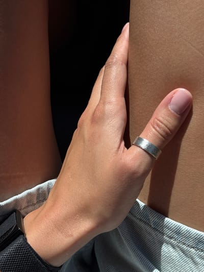 The image shows a close-up view of a person's hand resting on their thigh, with a portion of denim shorts visible at the bottom. The person is wearing a silver ring on their thumb and a black watch on their wrist. The lighting suggests an outdoor setting, possibly during daytime, with shadows cast on the skin. There are no discernible elements in the image that can be used to identify a specific location in Babljak, Montenegro.