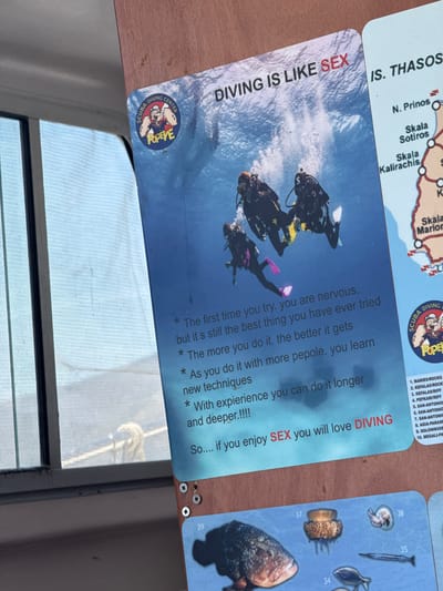 The image shows a close-up view of a blue poster mounted on a wooden surface. The poster features a photograph of three scuba divers underwater. Text on the poster reads "DIVING IS LIKE SEX". Below this, a list of bullet points describes the experience of diving. The bottom of the poster shows a list of dive sites, with numbers corresponding to locations on an accompanying map. The visible portion of the map lists locations such as "N. PRİNOS", "SKALA SOTİROS", and "SKALA KALİRACHİS", which are all located on Thassos Island. One of the bullet points reads, "So.... if you enjoy SEX you will love DIVING". In the upper left corner of the poster, a circular logo depicts Popeye the Sailor and reads "SCUBA DIVING CENTER POPEYE". To the right of this poster, another poster with map details is partially visible. The background suggests the image was taken outdoors, possibly on a boat or near water, given the reflective surface and the presence of a window with a sheer curtain. There is no explicit indication of the city of Potos, Greece in the image, but the map details point to Thassos Island, where Potos is located.
