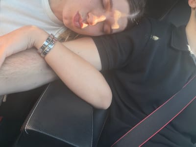 A person is reclining in a car. The person is wearing a black shirt, a white shirt, and a silver watch. They are also wearing a seatbelt. The car has black leather seats. It is not possible to determine if the image was taken in Barakovo, Bulgaria.