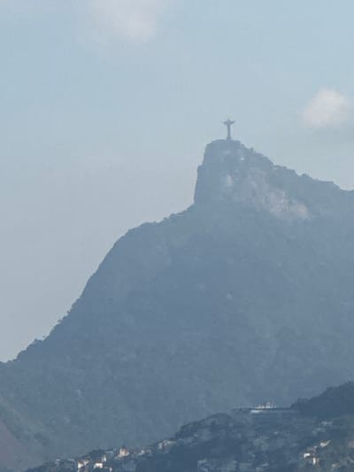 A statue of Jesus Christ, known as Christ the Redeemer, stands atop Corcovado Mountain in Rio de Janeiro, Brazil. The statue, made of soapstone and concrete, is 30 meters (98 feet) tall and has an arm span of 28 meters (92 feet). It is situated at an elevation of 710 meters (2,330 feet) above sea level, overlooking the city. The statue is a global icon of Christianity and a symbol of Brazil. In the foreground, a dense cityscape with white buildings is visible nestled on the slopes of the mountain. The overall atmosphere of the image is serene and majestic, capturing the grandeur of both the natural landscape and the iconic statue.