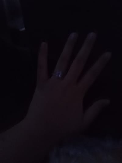 The image shows a close-up of a person's hand against a dark background. A ring with a clear gemstone is visible on the ring finger. The lighting is dim, obscuring many details of the environment and the person's features. The image does not provide any information about the city of Kaysar, Kyrgyzstan, or any other geographical context.