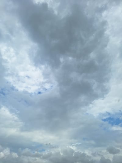 The image shows a cloudy sky with patches of blue visible in the distance. The clouds are varied in density and color, ranging from light gray to dark gray, with some areas appearing almost white. The lighting suggests it is daytime, but the heavy cloud cover indicates overcast or partly cloudy conditions. There are no people, structures, or discernible landmarks visible in the frame, making it impossible to determine a specific location within ჩიბათის თემი, Georgia, or any other city. The scene is purely atmospheric, focused on the natural phenomenon of cloud formations against a sky backdrop.
