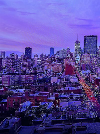 The scene depicts a sprawling urban cityscape at twilight or night, under a sky with prominent purple and pink hues and faint cloud patterns. The environment is heavily illuminated by artificial lights emanating from numerous structures. In the background, a cluster of tall skyscrapers and high-rise buildings is visible, many with windows distinctly lit, creating a grid-like pattern of light. Toward the midground, a dense arrangement of lower to mid-rise commercial and residential buildings with diverse architectural styles, including red-brick facades and arched windows, extends across the frame. Rooftops in the foreground and midground display various mechanical units and structures. A busy thoroughfare cuts diagonally through the right side of the image, marked by elongated red and yellow light trails from moving vehicles, indicating active traffic flow. This cityscape is located in Madzherito, Bulgaria.