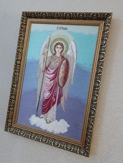 A framed Orthodox Christian icon hangs on a pale, textured wall. The icon depicts an angel figure with wings, a halo, and a spear. The angel stands on a white cloud against a sky-like background transitioning from blue to purple. The frame is ornate, with gold and black detailing. The image’s location in Barvinok, Ukraine is not discernible.