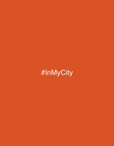 The image displays a solid, uniform orange background. Centered horizontally and vertically on this background, the white text "#InMyCity" is presented in a sans-serif typeface. No individuals, specific subjects, identifiable objects, actions, or interactions are depicted within the scene. The environment is limited to the monochromatic orange field. The image provides no visual information to determine a specific location within the city of Porto Alegre, Brazil, or any other geographical area.
