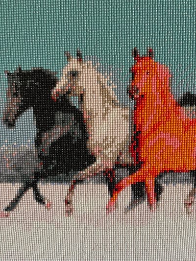 The image depicts a diamond painting of three horses in profile against a teal background. The horse on the left is black, the middle horse is white with pink accents, and the horse on the right is orange with pink accents. The horses are in motion, with their legs blurred as if running. The diamond painting is rendered in a mosaic style, with each individual diamond visible. There is no discernible location in the city of Мяндиги, Russia.