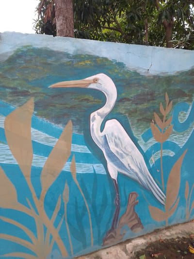 Mural painted on a wall. The subject is a white egret standing in water. The painting depicts various plants. The background shows what appears to be hills and water. Located in Villa Hayes, Paraguay.