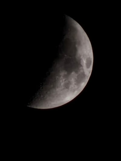 The image presents the Moon in a distinct first or third quarter phase, with precisely half of its visible disk illuminated, set against a completely black, starless sky. The illuminated lunar surface reveals numerous impact craters and darker, smooth maria. The sharp terminator line clearly delineates the illuminated portion from the unlit area. No other celestial bodies, atmospheric phenomena, or terrestrial structures are discernible within the frame. This astronomical observation was recorded from the location of ქვედა სამება, Georgia.