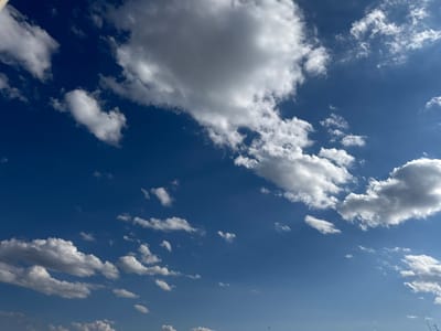 This is a photograph of a bright blue sky with scattered white clouds. Several small, dark shapes that appear to be birds are visible flying in the sky. The image was taken in Slobozhanske, Ukraine.