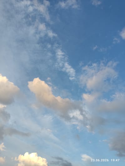 This is a photograph of a sky filled with clouds. The sky is a vibrant blue, transitioning to lighter shades towards the horizon. Several types of clouds are visible, including wispy cirrus clouds and larger, more defined cumulus clouds. Some of the cumulus clouds are illuminated by sunlight, appearing bright white and golden, while others are darker and shadowed. The scene suggests a pleasant day with a mix of sunny and cloudy conditions.

A timestamp is overlaid on the right side of the image, reading "23.06.2026 19:47". This indicates the photograph was taken on June 23, 2026, at 7:47 PM. The time and the angle of the sunlight hitting the clouds suggest it is late afternoon or early evening, likely close to sunset.

There are no people or specific objects visible in the frame, focusing solely on the natural spectacle of the sky. The location context provided is Kuyuki, Russia, which, when combined with the time of year and day, might imply a specific atmospheric condition or view common to that region. The overall emotion evoked by the image is one of calm and vastness, a common feeling when observing a wide expanse of sky.