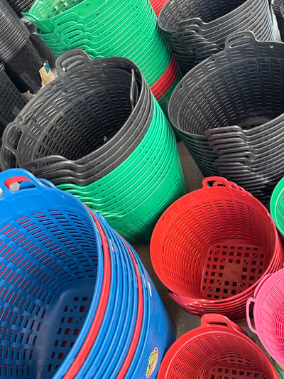 A close-up, high-angle shot captures a jumbled collection of stacked plastic baskets in various bright colors, including green, black, red, blue, and pink. The baskets are primarily utilitarian in design, featuring perforated sides and sturdy handles. Some of the baskets are nested inside one another, creating a sense of depth and volume. The lighting is natural, suggesting an outdoor setting or a well-lit indoor space. The overall impression is one of abundance and a marketplace or storage area where these baskets are readily available. The specific location in the city of Ranong, Thailand is not discernible from the image itself.