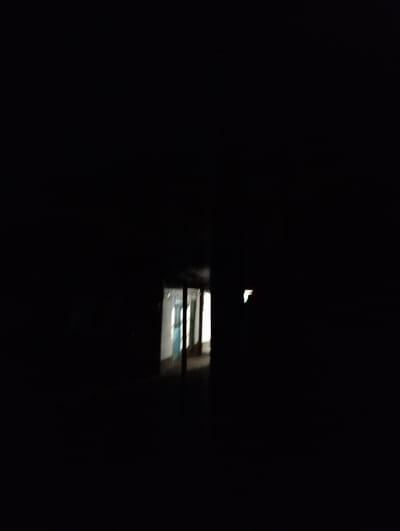The image depicts a dark, narrow hallway with a faint light emanating from the end. The hallway appears to be part of an abandoned or disused building, possibly a school or dormitory, given the presence of what looks like lockers or cubbies along one side. The lighting suggests it is nighttime or the area is unlit. The scene evokes a sense of mystery and desolation. There is no visible text in the image. The location is identified as Қарғалы, Kazakhstan.