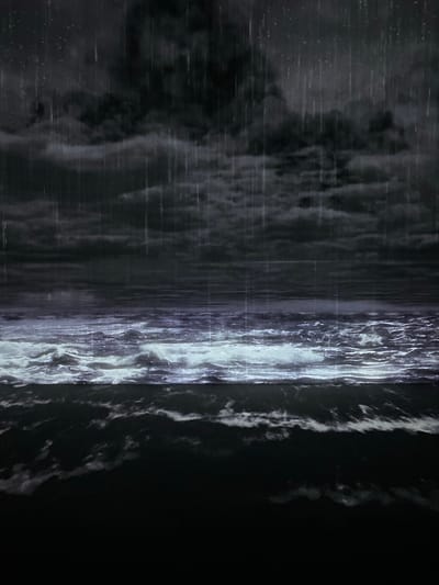 The image depicts a stormy scene at sea, possibly in Pattaya City, Thailand. Heavy rain falls from dark, ominous clouds, creating streaks of light against the dark sky. The choppy ocean waves are illuminated by an unseen light source, giving them a turbulent, almost ethereal appearance. The lower portion of the image is dominated by the dark, foreboding sea. There are no people or man-made structures visible in the scene, emphasizing the raw power of nature.