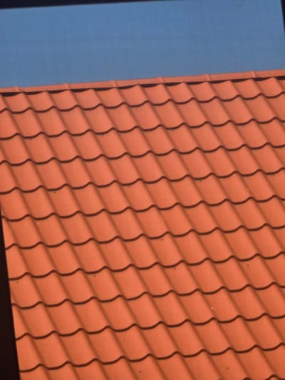 The image shows a close-up of an orange tiled roof against a clear blue sky. The tiles are wavy in shape, creating a repetitive pattern. There are some small dark spots visible on the tiles, which appear to be shadows or possibly minor imperfections. The image is taken from an upward angle, suggesting the viewpoint is from below the roof. There is a dark horizontal line across the top of the image, possibly the edge of another structure or the frame of the photograph. No people or any other objects are visible. The location in Avtury, Russia is not discernible from the visual information alone.