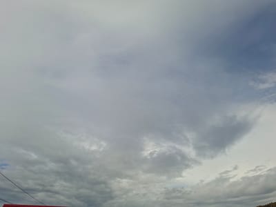 The image depicts a cloudy sky over the city of Karakasly, Russia. A thin black wire stretches diagonally across the lower left quadrant of the image. In the bottom left corner, a portion of a red structure, possibly a building or fence, is visible. The sky is filled with a variety of clouds, ranging from light, wispy formations to heavier, darker masses, suggesting a somewhat overcast or changing weather condition. The overall impression is one of an outdoor scene on a day with diffused light.