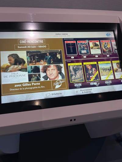 The image shows a close-up of a cinema ticketing kiosk screen. The screen displays movie posters and showtimes. The top of the screen indicates "FAMILY CINEMA" and the date "vendredi 12 juin 2026 - 18:31". Below this, it says "Séances immédiates" (Immediate showings). A large central graphic promotes a "CINÉ-RENCONTRE" (Film Encounter) event with "Samedi 20 Juin - 18h00" and features a poster for the film "FILS DE PERSONNE" with director of photography Gilles Porte.

Below the "Séances immédiates" section, there are several movie posters for films like "La Bataille de Gaulle...", "Scary Movie", "Fils de personne", "Star Wars: The Man...", and "L'A...". Further down, under the heading "À la une" (On the front page), there are more film listings with showtimes for "Ven. 12 Juin - 19:00", "Lun. 15 Juin - 20:30", "Jeu. 18 Juin - 20:30", and "Sam. 20 Juin".

At the bottom of the screen, there is a section for "Abonnement & Fidélité" (Subscription & Loyalty) and a button for "Billetterie" (Ticketing). The kiosk itself is white with a black bezel around the screen. The overall environment appears to be indoors, likely within a cinema lobby. There is no information in the image that specifies a location in the city of Saint-Just-Saint-Rambert, France.