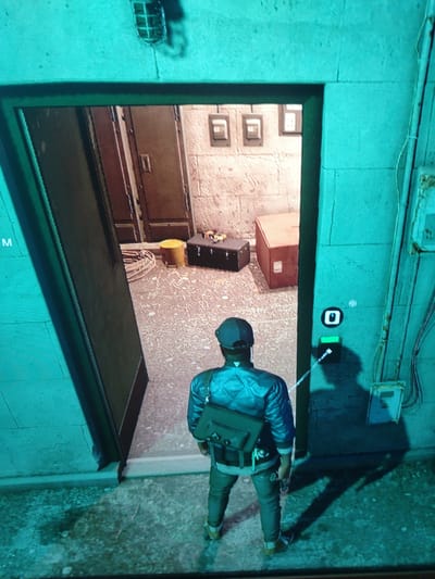 In an overhead shot, a person wearing a dark blue jacket with a diamond pattern, a black baseball cap, and grey pants stands facing away from the viewer. They have a black messenger bag slung over their right shoulder and are holding something in their right hand. They are positioned at the entrance of a doorway leading into a room.
The room beyond the doorway has a textured, light-colored floor and walls. Inside, there are several objects: a dark-colored trunk, a bright yellow cylindrical object, a large orange box, and what appears to be a rolled-up mat or rope. The walls are adorned with three square frames containing what look like electrical outlets or light switches. Further in, there is a closed wooden door.
The exterior area features a rough, concrete-like floor. On the right side of the doorway, mounted on the wall, is a black electrical box with a white circular symbol above it, and below that, a green illuminated panel with a black button. A thin white cord extends from the green panel towards the person. The overall lighting has a strong teal-blue cast, suggesting artificial lighting or a filter. The environment appears to be within the city of Buynichi village council, Belarus.