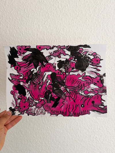 The media file displays a piece of abstract art held by a person's hand against a textured white wall. The artwork features bold strokes of pink and black paint on a white background. The style is expressive and somewhat chaotic, with organic shapes and thick lines. The pink elements are vibrant and vary in intensity, with some areas appearing more solid and others more translucent or streaky. The black paint is applied in a more graphic manner, outlining some of the pink shapes and filling in others to create darker masses. There are suggestions of figures or creatures within the abstract composition, with some elements resembling eyes or mouths. The overall impression is one of energetic movement and a sense of playful or perhaps unsettling imagery. The person's hand, holding the bottom right corner of the artwork, is visible and appears to be in a casual grip. The wall behind is a uniform white with a distinct, bumpy texture, suggesting it is an interior surface. There are no discernible landmarks or cues that would indicate the specific location beyond the general context of Nienburg/Weser, Germany. The lighting appears to be even and diffused, without strong shadows, indicating it might be natural light or well-lit indoor conditions. No text is visible on the artwork or in the scene.