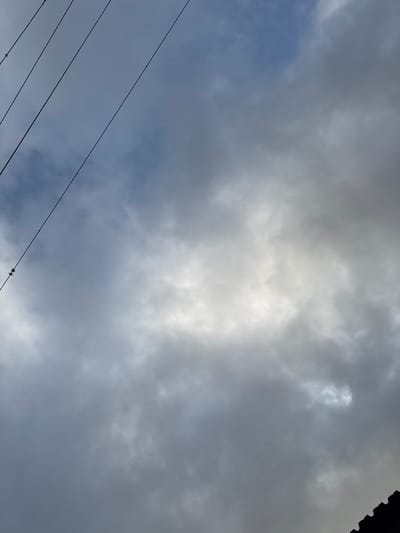 The image depicts a cloudy sky with overcast conditions. The clouds are primarily gray and white, suggesting a potentially stormy or rainy day. A set of power lines diagonally crosses the lower-left portion of the image. There is a hint of a dark structure, possibly a roof, in the upper-right corner. The location is potentially the city of Parroquia Ocumare, Venezuela.