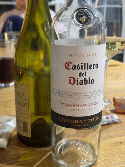 The image shows two wine bottles lying on a wooden surface. The top bottle is a "Casillero del Diablo" Sauvignon Blanc from Chile, vintage 2025, produced by Concha y Toro. The bottom bottle is green glass with a label partially visible, displaying the word "LLAGES". The image doesn't provide enough information to determine the location in Craigavon, United Kingdom.