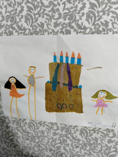 The image is a drawing on white paper, with a patterned fabric background. The drawing depicts a birthday cake with candles, and three stick figures of people. One figure on the left has long black hair and an orange dress. Another figure in the center is taller, with an orange body, grey torso, and a halo. A third figure on the right has green hair, a pink dress, and orange legs. The cake is brown with blue and purple decorations. Below the drawing, in blue ink, are the words "Лера 20262 5,92 20.02.24" and a drawing of a flag. There is no information within the image to indicate a specific location in the city of Luhansk, Ukraine.