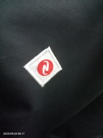 A close-up photograph captures a section of black woven textile material, likely synthetic. A white, diamond-shaped embroidered patch is centrally affixed to the material. The patch features a red, stylized letter 'N' or similar symbol, centrally enclosed within a red oval. No individuals are present, and no actions or interactions are depicted. The scene is identified as Quebrada del Medio, Venezuela. A digital watermark in the lower-left corner indicates a capture date and time of 2025/09/24 08:17.