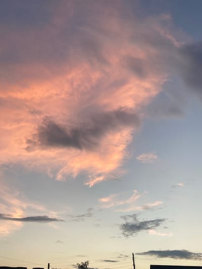 This image captures a dramatic sunset over a rural landscape in Mamontovo, Russia. The sky is a canvas of soft blues, fading into a pale yellow and peach hue near the horizon. Wispy clouds, tinged with pink and orange from the setting sun, stretch across the frame, creating a dynamic and painterly effect. Some darker, more defined clouds are interspersed, adding depth and contrast to the scene.
On the right side of the image, a utility pole with power lines is visible, suggesting the presence of a nearby settlement or infrastructure. The faint silhouette of trees can be seen in the distance. The overall mood is serene and tranquil, with the warm colors of the sunset evoking a sense of peace and natural beauty. The time of day is clearly sunset, indicated by the low angle of the sun and the vibrant colors in the sky. The weather appears clear, with only scattered clouds. No text is visible in the image.