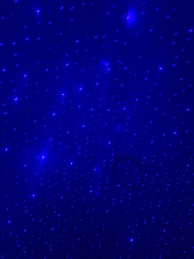 The image is a close-up, abstract view of a dark blue surface illuminated by numerous small, bright blue and purple lights, resembling stars in a night sky. Some lights appear as short streaks, while others are more like dots. There is a faint, circular shadow or obstruction visible in the upper right quadrant of the image, with a soft-edged outline. The overall impression is of a projected light display. The image does not contain any discernible landmarks or context to suggest a specific location within Tijuana, Mexico.