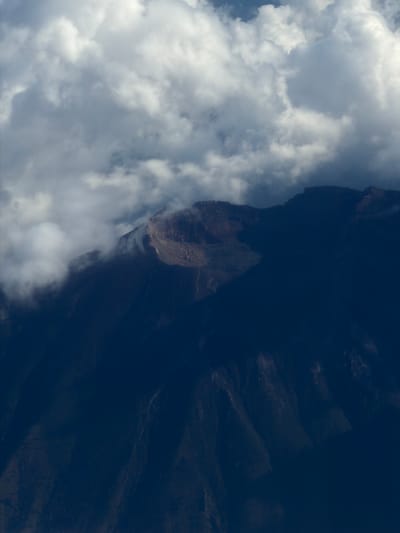 The image shows a partially obscured view of a mountain range shrouded in cloud cover. The mountain appears dark and rugged, with visible rock formations and shadows. The clouds are predominantly white and gray, suggesting varying densities and altitudes. The overall orientation of the image is such that the mountain range runs vertically along the right side, while the clouds are primarily located on the left. Without additional information, it's not possible to confirm a specific location within Taoyuan City, Taiwan.