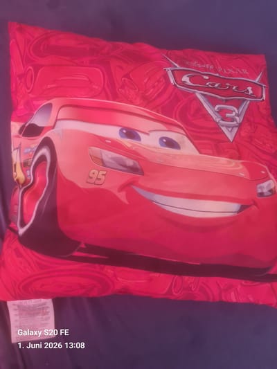 The image shows a red square pillow with a print of Lightning McQueen from the Disney Pixar movie "Cars". The pillow is placed on a dark blue surface. A tag is visible on the bottom right corner of the pillow. The date and time "1. Juni 2026 13:08" are printed on the lower right side of the image, indicating when the photo was taken. The location is not mentioned in the image, and there is no indication that the photo was taken in Bingen am Rhein, Germany.