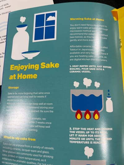 The image shows a page from a pamphlet titled "Enjoying Sake at Home" with information on how to warm sake at home. The pamphlet uses illustrations of a ceramic sake vessel, a burner, and a bottle of sake to visually guide the user through the process. The text describes the recommended method of heating the sake using boiling water, and advises against using a microwave. The pamphlet also provides information on the storage of sake and different vessels used to drink sake. The pamphlet is printed on a blue background, with the heading "Enjoying Sake at Home" in bold, black lettering. The latitude and longitude coordinates given are irrelevant to the image as the pamphlet doesn't provide any geographic location information.