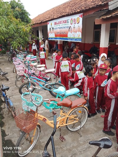 A group of children, dressed in matching red and white uniforms, stand in front of a building with a banner that reads "DIRGAHAYUPGRI" and "HARI GURU NASIONAL TAHUN 2025." Several bicycles, some with baskets, are parked nearby. The scene is captured with a smartphone camera, as indicated by the "Vivo Y19s" watermark in the corner, along with the date "10 Nov 2025, 07:32."