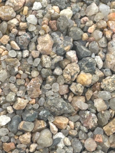 This is a top-down, close-up, eye-level shot of a dense accumulation of various sized gravel stones. The stones are predominantly muted earth tones, with shades of grey, beige, tan, and some lighter white and reddish-brown flecks. Their textures vary from smooth and rounded to rough and angular. The lighting appears even, suggesting it's either overcast or taken in diffused light, with no harsh shadows. The scene is a still-life composition of natural elements. No people, specific objects, or discernible text are present. The setting is a collection of natural stones, indicative of a ground surface or a pile of aggregate material. The image is likely a detail shot, focusing solely on the texture and composition of the gravel. Given the location context of Володарский ауылдық округі, Kazakhstan, this could be a representation of local terrain, construction material, or natural ground cover.