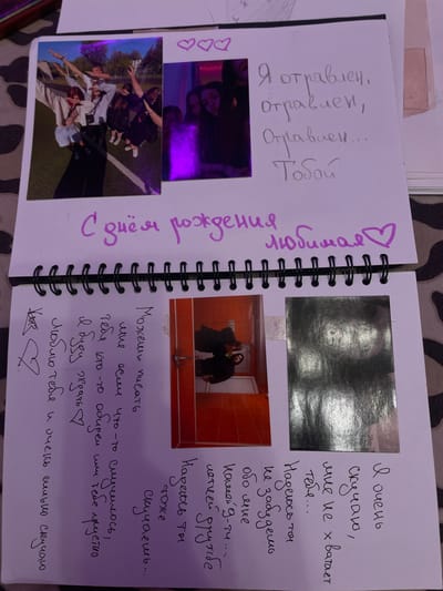 The image displays an open spiral-bound notebook with handwritten text and photographs. The notebook is laid flat on a surface with a camouflage pattern. On the right page, there are three pink heart outlines at the top, followed by handwritten Russian text in grey ink. The text reads: "Я отравлен, отравлен, Отравлен... Тобой" which translates to "I am poisoned, poisoned, Poisoned... By you." Below this text is a photograph of a person, possibly indoors.
The left page of the notebook features a large photograph on the top left showing a group of young people posing outdoors, with one person appearing to be doing a "dab" pose. To the right of this photograph is a smaller, vertically oriented photograph with a purple glow, showing two individuals. Below these photographs, a heading in large purple cursive text reads "С днём рождения любимая ♡" which translates to "Happy birthday my love ♡".
Further down the left page, there is a drawing of a stylized heart with an arrow through it. To the right of this drawing is a column of handwritten Russian text in black ink. The text appears to be a personal message or poem, including phrases like "Можешь писать мне если", "тебя кто-то", "Я буду ждать", "люблю тебя" and "и очень сильно скучаю".
On the right side of the left page, starting from the bottom, there are more handwritten Russian text in black ink, which reads: "Я очень скучаю, мне не x хватает тебя... Надеюсь ты не забудешь обо мне какой-g-ту..." translating to "I miss you very much, I lack you... I hope you don't forget about me, any kind of..." This text is partially obscured by photographs.
There are two photographs on the lower portion of the right page. The left photograph shows two people in a room that appears to be a bathroom with orange tiles. The right photograph is a dark, reflective image, possibly a person's reflection or a highly glossy print.
The location of Ladozhskii Trudposelok, Russia, is not depicted or suggested in the image.