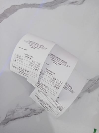 Four receipts are laying flat on a white tiled surface. All four receipts are from the Famous Line Hotel & Suites, located at No. 10, Ujevwu Road, off Okpanam Road, Ujevwu, Delta State. The receipt on the bottom left corner is dated 18/08/2023 12:28 PM and reads: “POS Customer,” “Description,” “2XBIG SEVEN,” “15% BLACK BULLLET,” “Gross,” “Amt Dropped,” “Net Amount,” “Sales Tax (5%),” “Total Amount.” The receipt on the right side of the image is dated 18/08/2023 12:28 PM and reads: “POS Customer,” “Description,” “2XBIG SEVEN,” “15% BLACK BULLLET,” “Gross,” “Amt Dropped,” “Net Amount,” “Sales Tax (5%),” “Total Amount.” The top two receipts are slightly folded and do not provide any details. The receipts all include a "Rate" and "Amt" column for their prices. The receipts are blank in all areas except the header and the bottom sections.