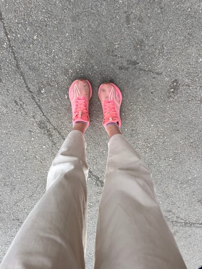 A person is standing on an asphalt surface, likely a street or sidewalk. They are wearing beige pants and pink running shoes. The location is Bol'shaya Sosnova, Russia. The weather appears to be overcast, as the lighting is even.