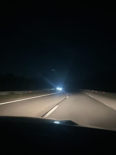 The image shows a structure illuminated by white lights at night. The structure appears to be concrete or a similar material, with linear elements suggesting a road or path. To the left of the structure is darkness and the sky is visible. Red lights can be seen on the edge of the structure. The scene seems to be in Blajievo, Bulgaria based on the instructions, though there is no visual information in the photo that indicates the location.