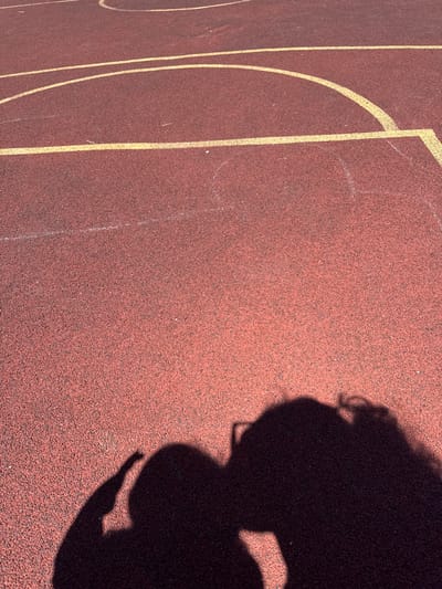 The image shows a shadow of two people on a red running track. The track has yellow lines indicating lanes. The shadows suggest that one person is wearing glasses. The lighting indicates it is daytime. The location in the city of Вязники, Russia is not discernible from the image.