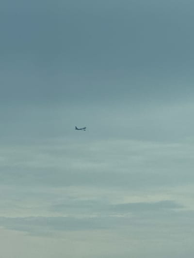 A faint, distant airplane is visible in a hazy, pale blue sky, slightly to the right of the center of the image. The sky is filled with diffuse, horizontal cloud formations. The overall impression is one of a vast, open sky with no discernible ground features. The location is the Khazar Raion, Azerbaijan.