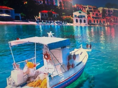 The image shows a boat in clear turquoise water with buildings in the background. The buildings appear to be in a coastal town, with red-tiled roofs and whitewashed walls. The water is calm and reflects the colors of the buildings and the sky. There are no people visible in the image. The boat is white with a blue stripe and has a canopy. It appears to be a small fishing boat. The scene is idyllic and peaceful. This image is not located in the city of Ellwangen, Germany.