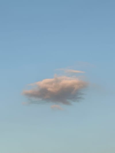 A single, small, light-colored cloud floats in a pale blue sky. The cloud is tinged with pink and gray hues, suggesting it is illuminated by sunlight. The vast expanse of the sky dominates the frame, with no visible land, structures, or other objects. The image appears to be a photograph taken from an outdoor location. The specific location in Завалочыцкі сельскі Савет, Belarus, cannot be determined from the visual information provided in the image.