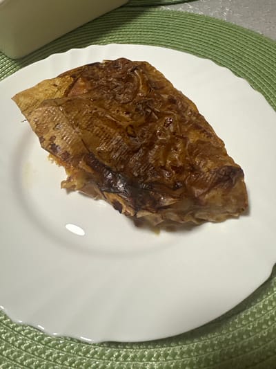 The image shows a piece of cooked food, possibly tofu skin, sitting on a white plate. The plate is placed on a green placemat, which is on a textured, possibly gray or white, surface. The location in the city of Vorotynsk, Russia is unknown and cannot be derived from this image. There are no people visible in the frame.