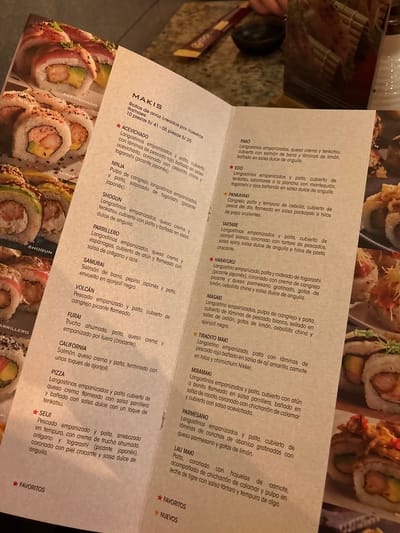 This media file displays a menu for a sushi restaurant, featuring various types of maki rolls. The menu is densely packed with text, listing the names and descriptions of different sushi creations, along with their prices. The backdrop of the menu is a photograph of several sushi rolls, artfully arranged and visually appealing. Some of the rolls are partially visible, showcasing their ingredients like avocado, shrimp, and sesame seeds. The overall presentation suggests a high-quality dining experience, with an emphasis on fresh ingredients and creative preparations. The menu text is in Spanish and includes names like "ACEVICHADO," "NINJA," "SHOGUN," and "CALIFORNIA," indicating a fusion of Japanese and Peruvian culinary influences. The prices are listed in Peruvian Soles (S/). The visual element of the sushi rolls adds to the appetite appeal of the menu.