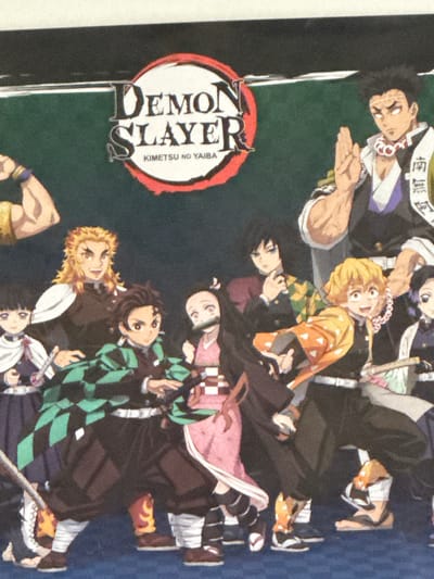 This media file appears to be a poster or illustration featuring characters from the anime series "Demon Slayer: Kimetsu no Yaiba." The subjects are a group of anime-style characters, predominantly young men, depicted in various poses. They are dressed in traditional Japanese attire, including kimonos and haori jackets.

One prominent object is a circular logo with stylized Japanese text and the English words "DEMON SLAYER" and "KIMETSU NO YAIBA" written vertically within it. The background is a dark, textured green, giving the impression of a night or dimly lit scene.

The characters are arranged in a dynamic composition, suggesting action or a gathering. Some characters have surprised or determined expressions. The overall mood is dramatic and energetic, consistent with the themes of the anime. There are no clear indicators of a specific time of day, weather, or geographical location beyond what is implied by the anime's setting. The clothing and hairstyles are distinctive to the series' characters.
