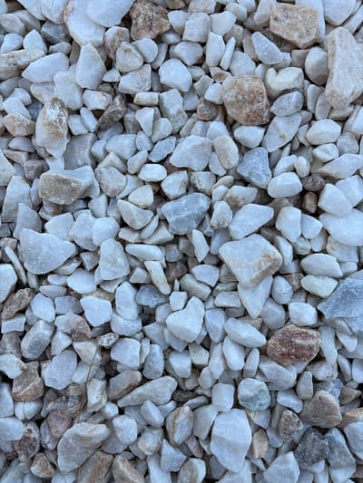 The image shows a close-up of small, irregularly shaped white and beige stones. The stones are densely packed, covering the entire frame. The environment appears to be a ground surface, possibly a pathway or decorative feature. The location is Municipal Unit of Elliniko, Greece. No people are visible in the image. There are no actions or interactions occurring.