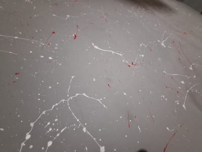 The image shows a gray surface spattered with red and white paint. The paint appears randomly distributed, with varying sizes and shapes of splatters, some forming drips and lines. No people, subjects, objects, actions, or interactions are visible other than the paint on the surface. The environment is limited to the gray surface with paint. No location information from Valchi Dol, Bulgaria, can be determined from the image.